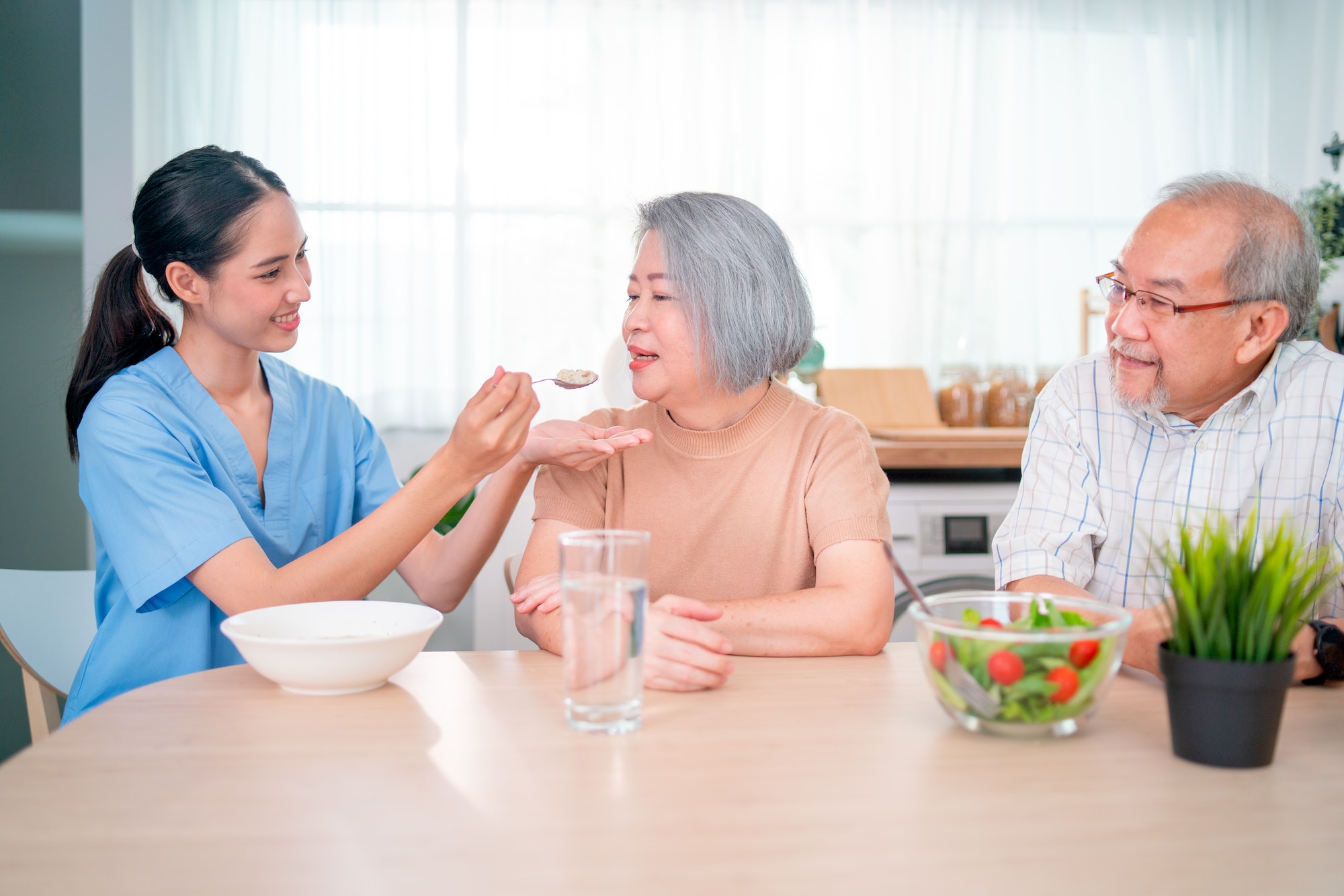 nurse-or-doctor-who-work-as-homecare-staff-help-to-serve-a-spoon-of-mush-rice-to-senior-woman